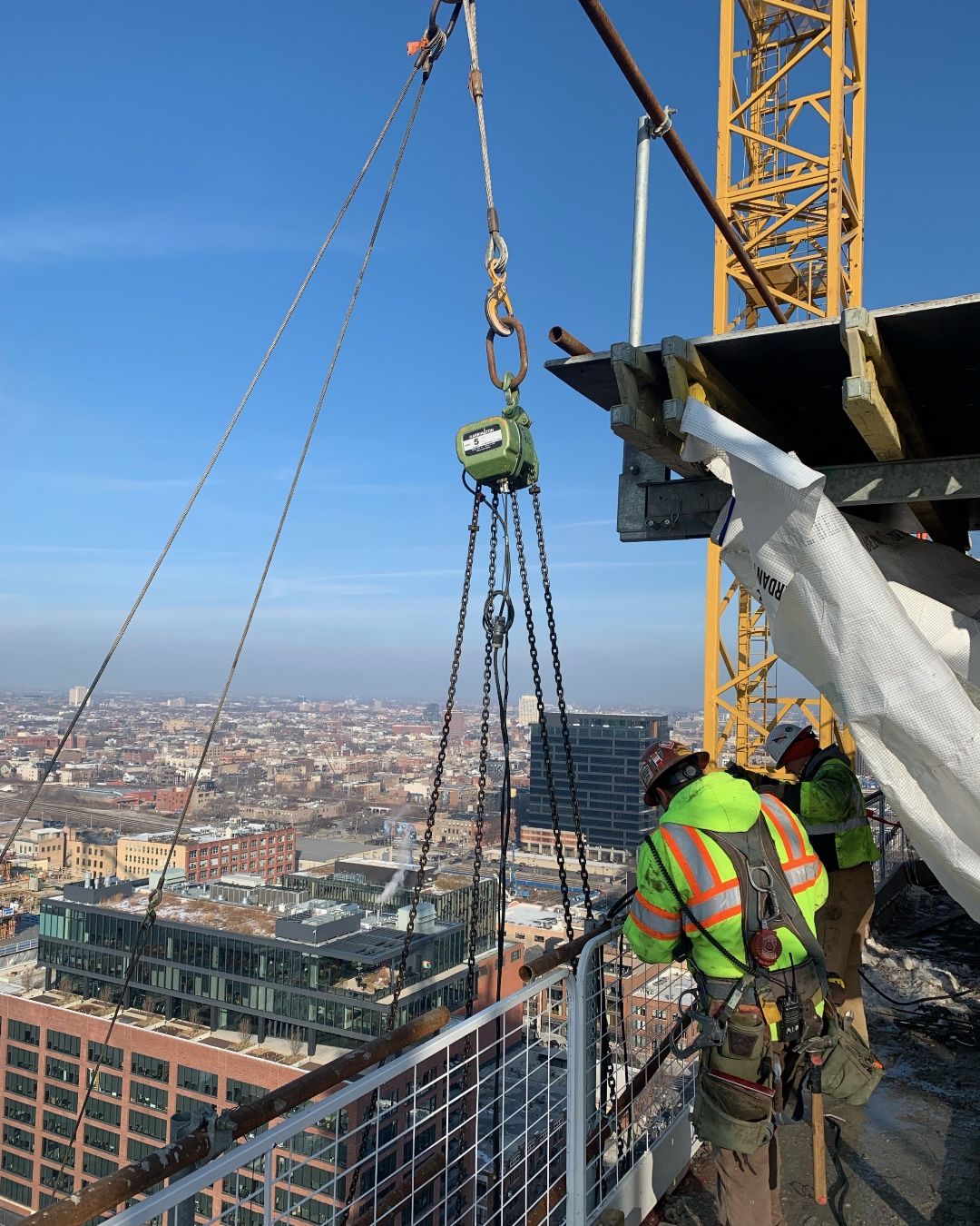 Jobsite photo of a 5 ton electric chain hoist with a construction worker on a platform.
